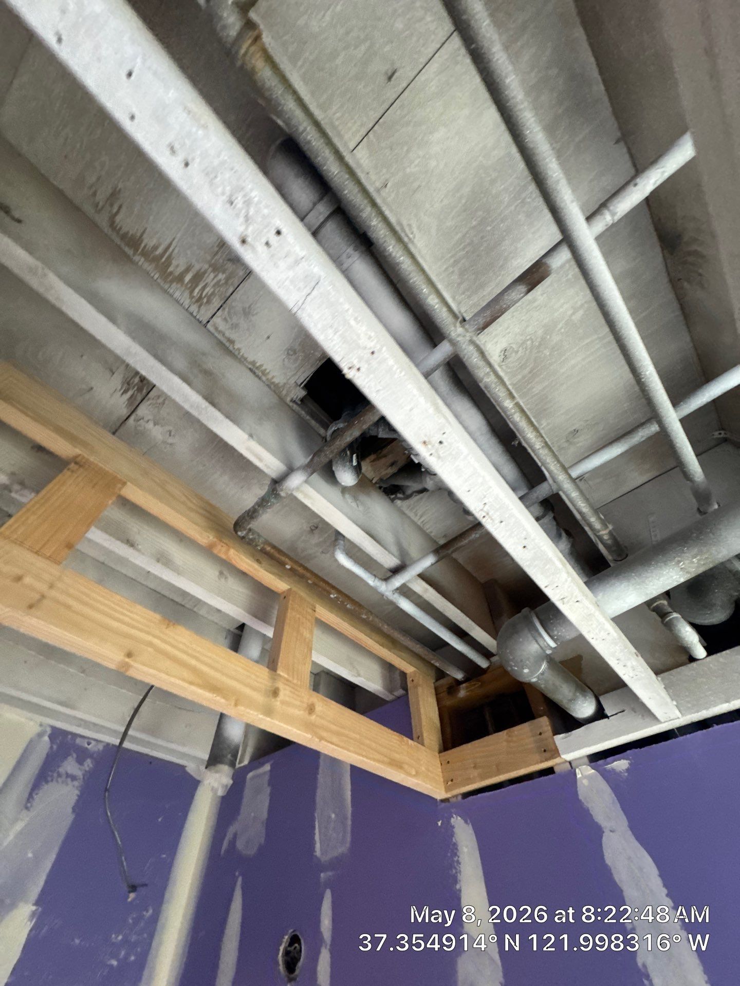 Exposed ceiling joists and ductwork above a purple wall in a room under construction