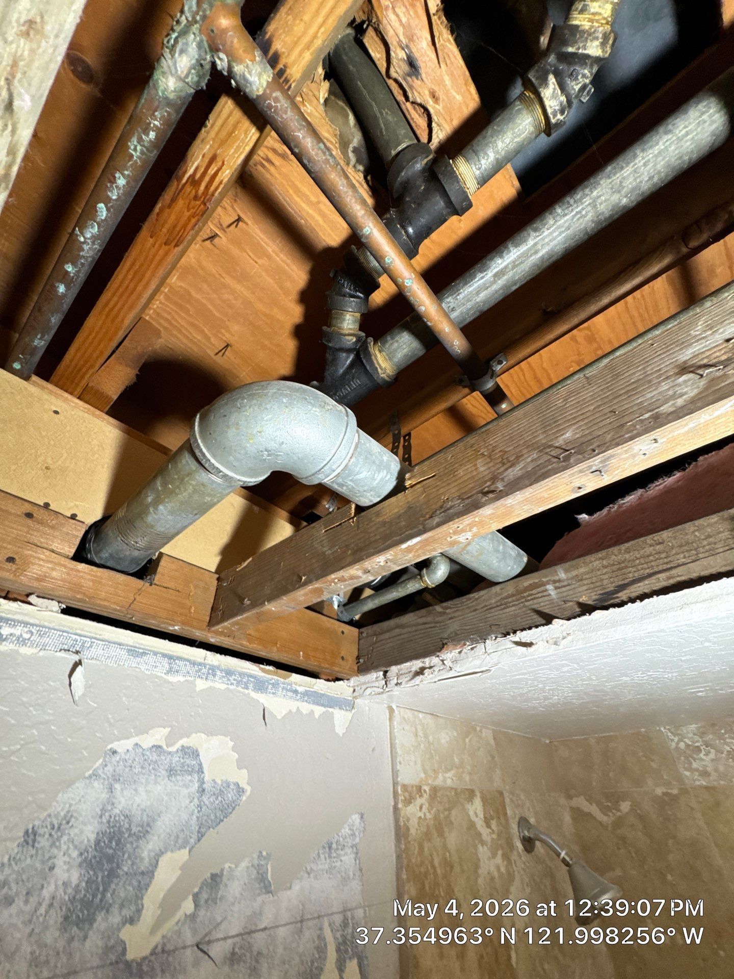 Exposed pipes and ductwork in a damaged ceiling above a water-stained room corner