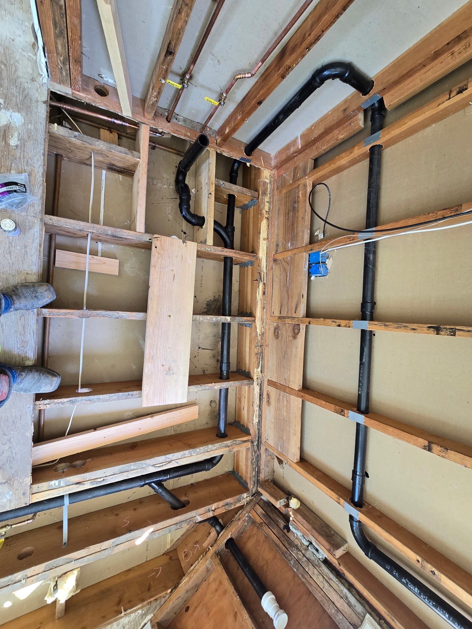 Interior construction framing with exposed wooden studs, black wiring, and unfinished drywall in a narrow stairwell.