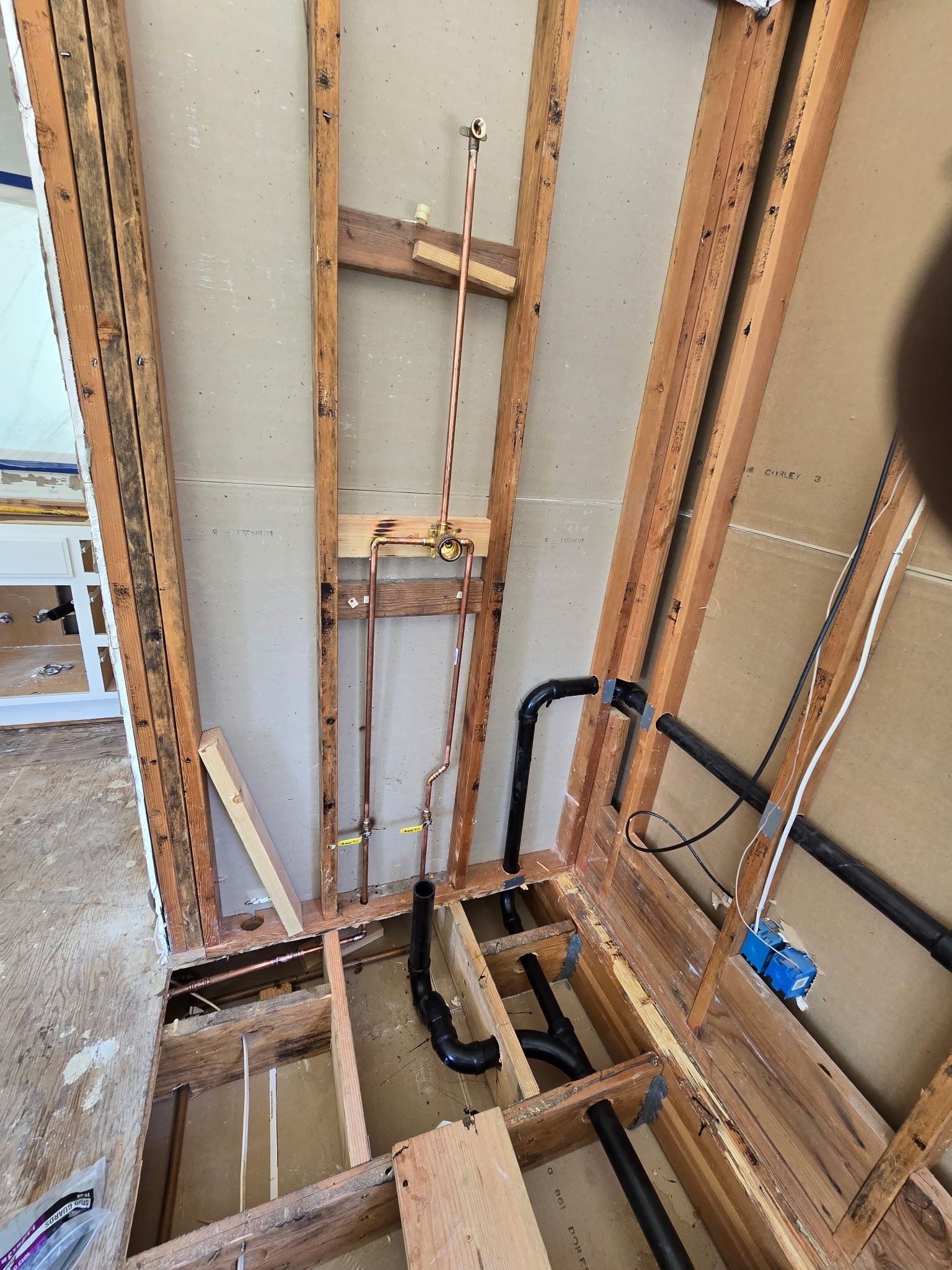 Exposed wall framing with pipes and wiring beside a utility shaft opening in a renovation area