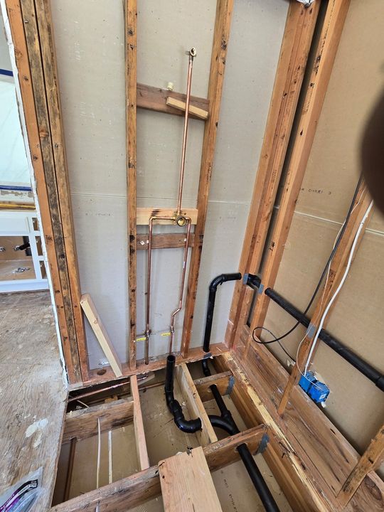 Partially demolished wall with exposed studs, wiring, and plumbing around a floor opening
