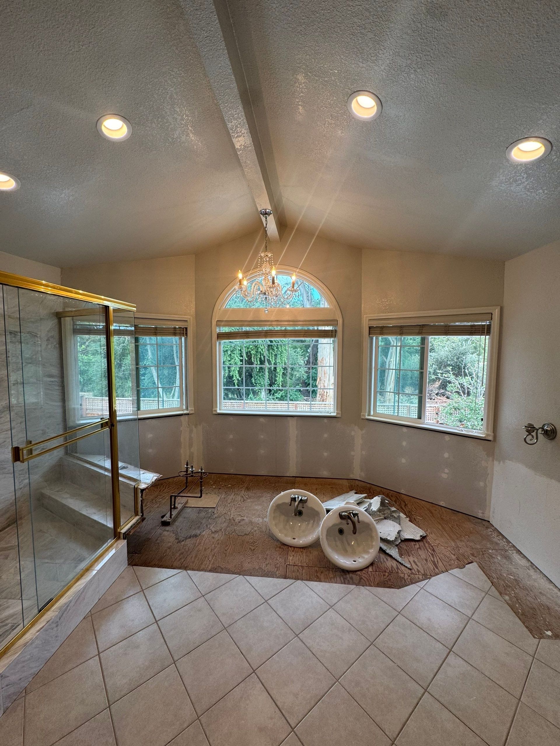 Empty tiled bathroom with a glass shower, three windows, and a brown bath mat on the floor.