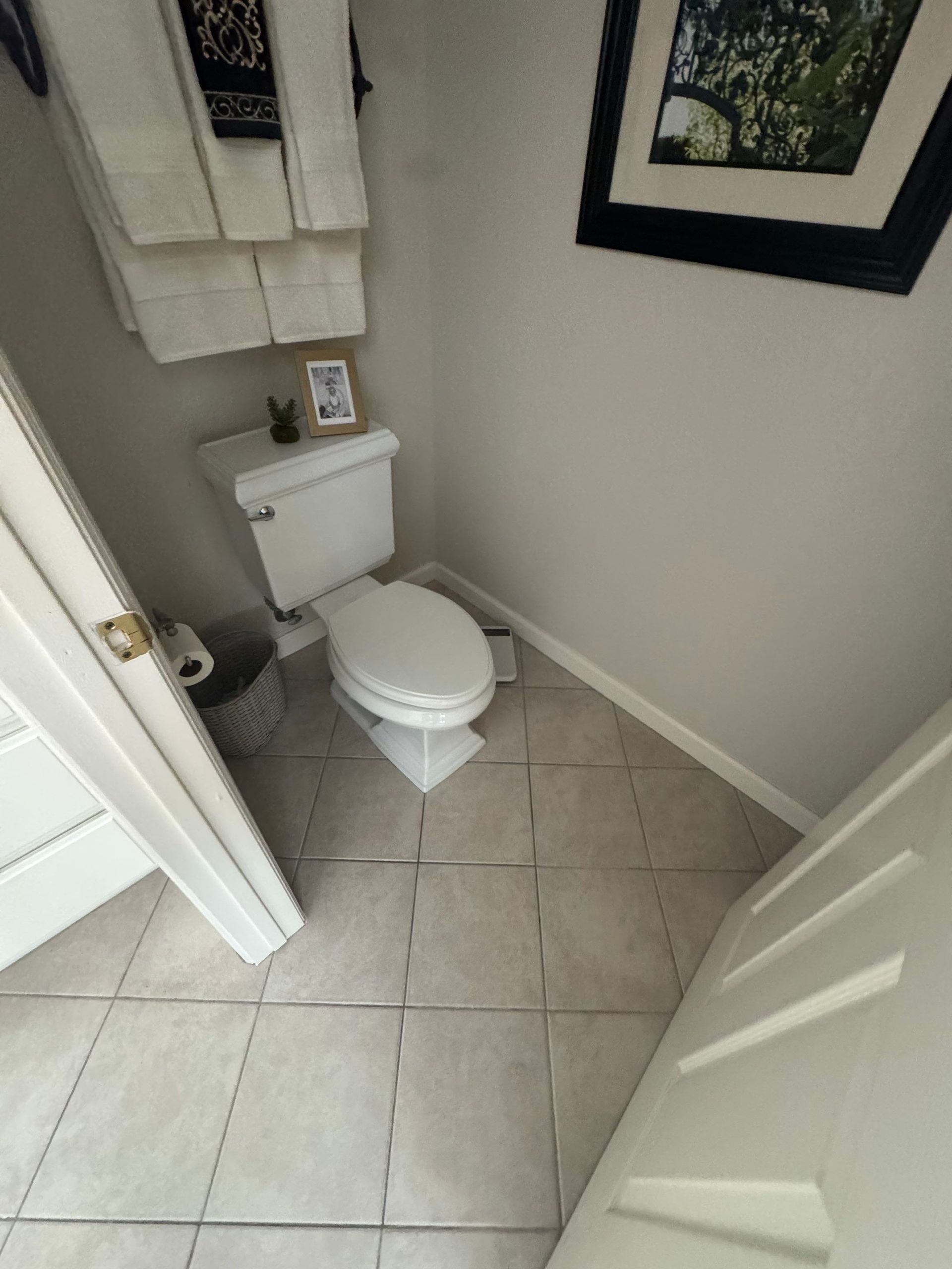 Small tiled bathroom with a toilet, beige walls, and a white towel above it