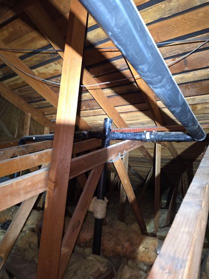 Wooden attic framing with a metal HVAC duct running through exposed rafters