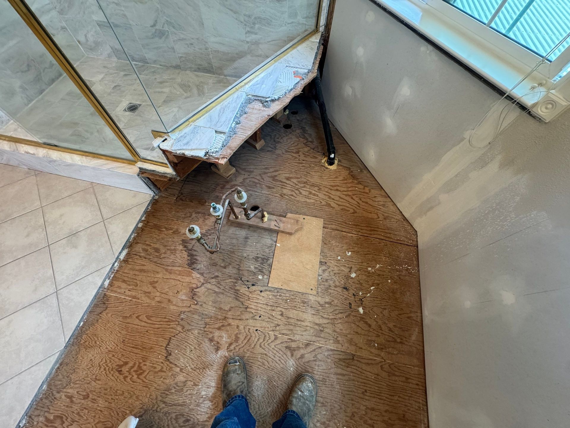 Damage around shower corner with broken tile, debris, and exposed floor beside a glass shower door