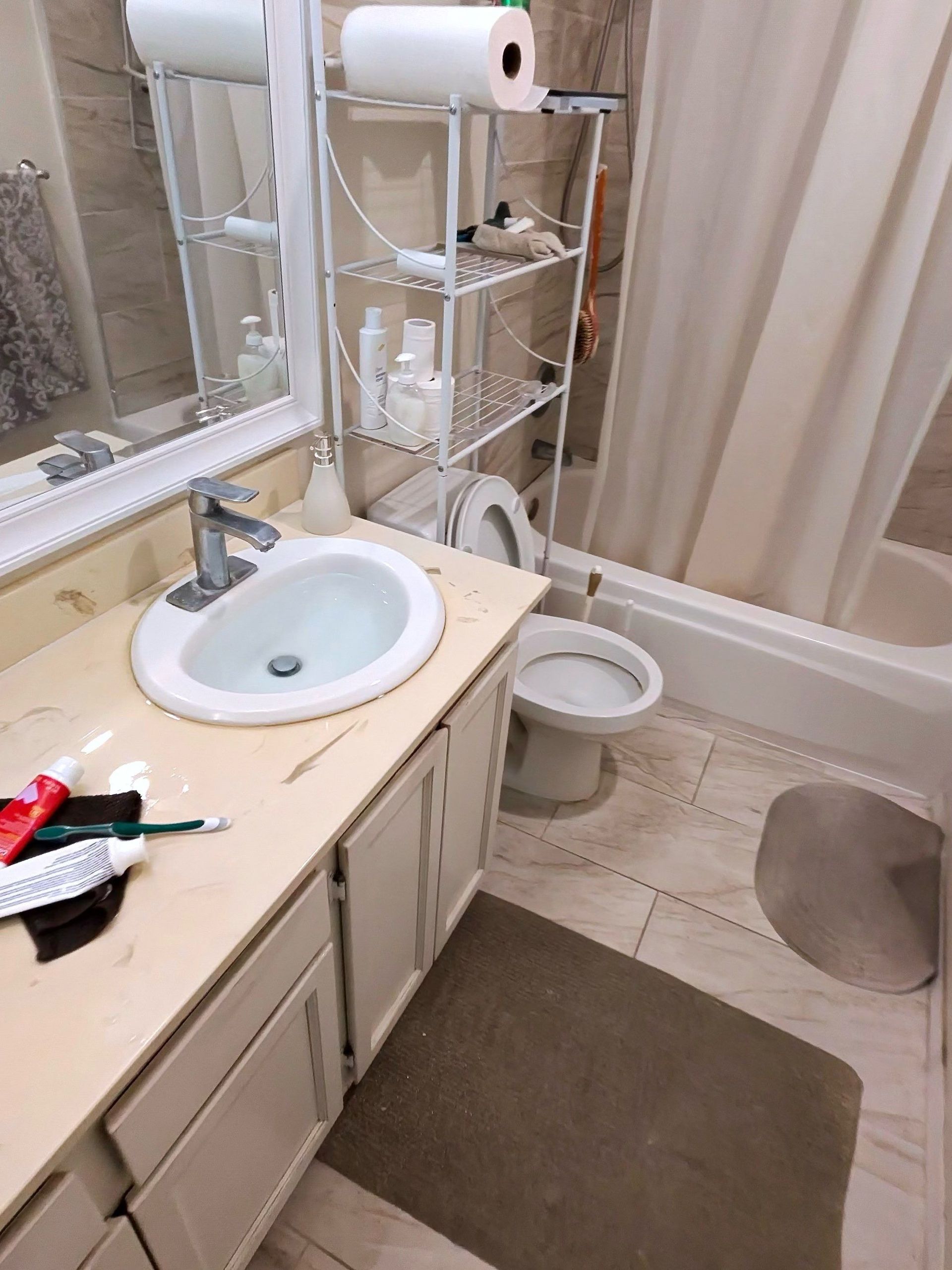 Small bathroom with sink, toilet, shower curtain, and toilet paper roll holder above the sink.