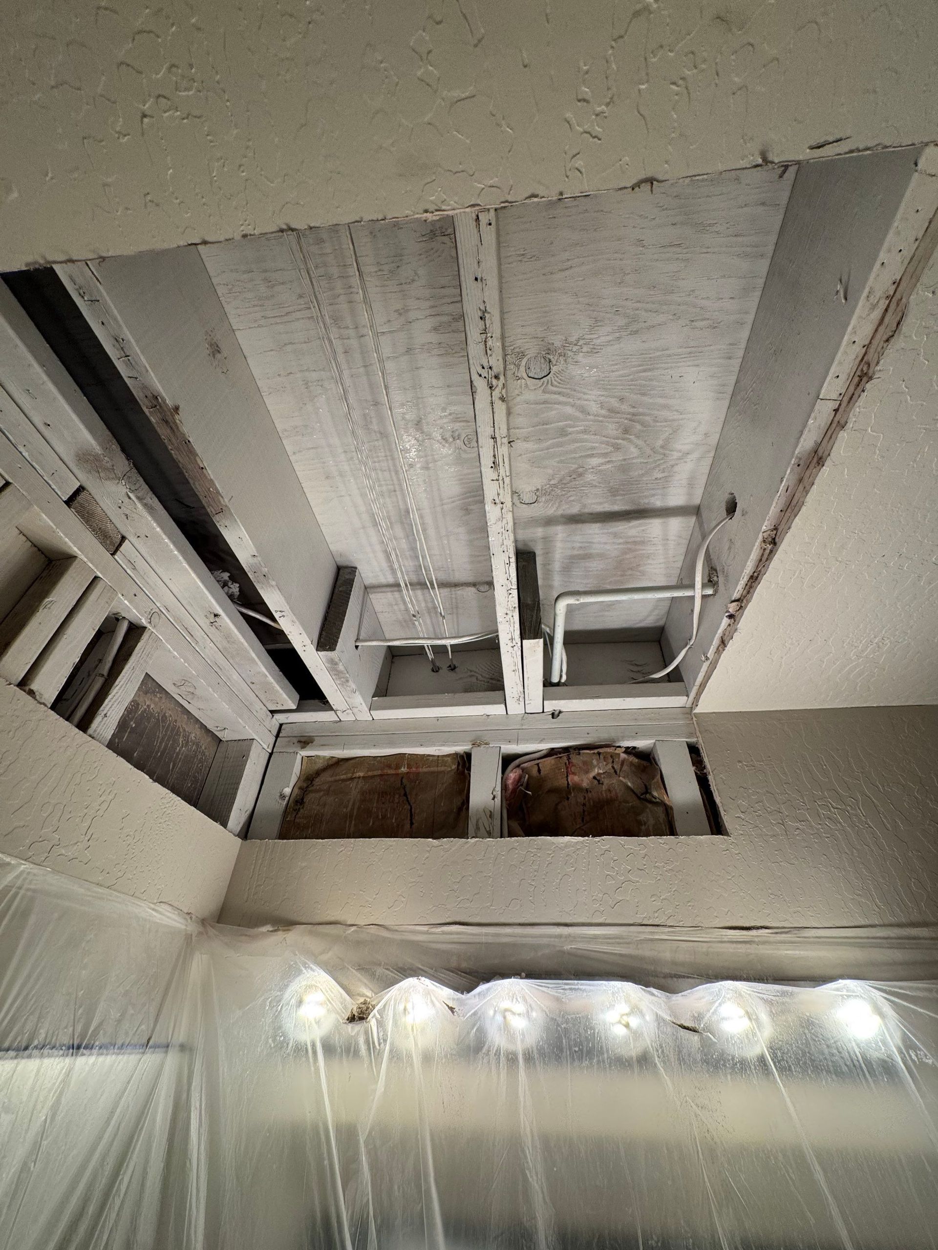 Damaged ceiling with exposed wooden framing and hanging plastic sheeting in a room under repair