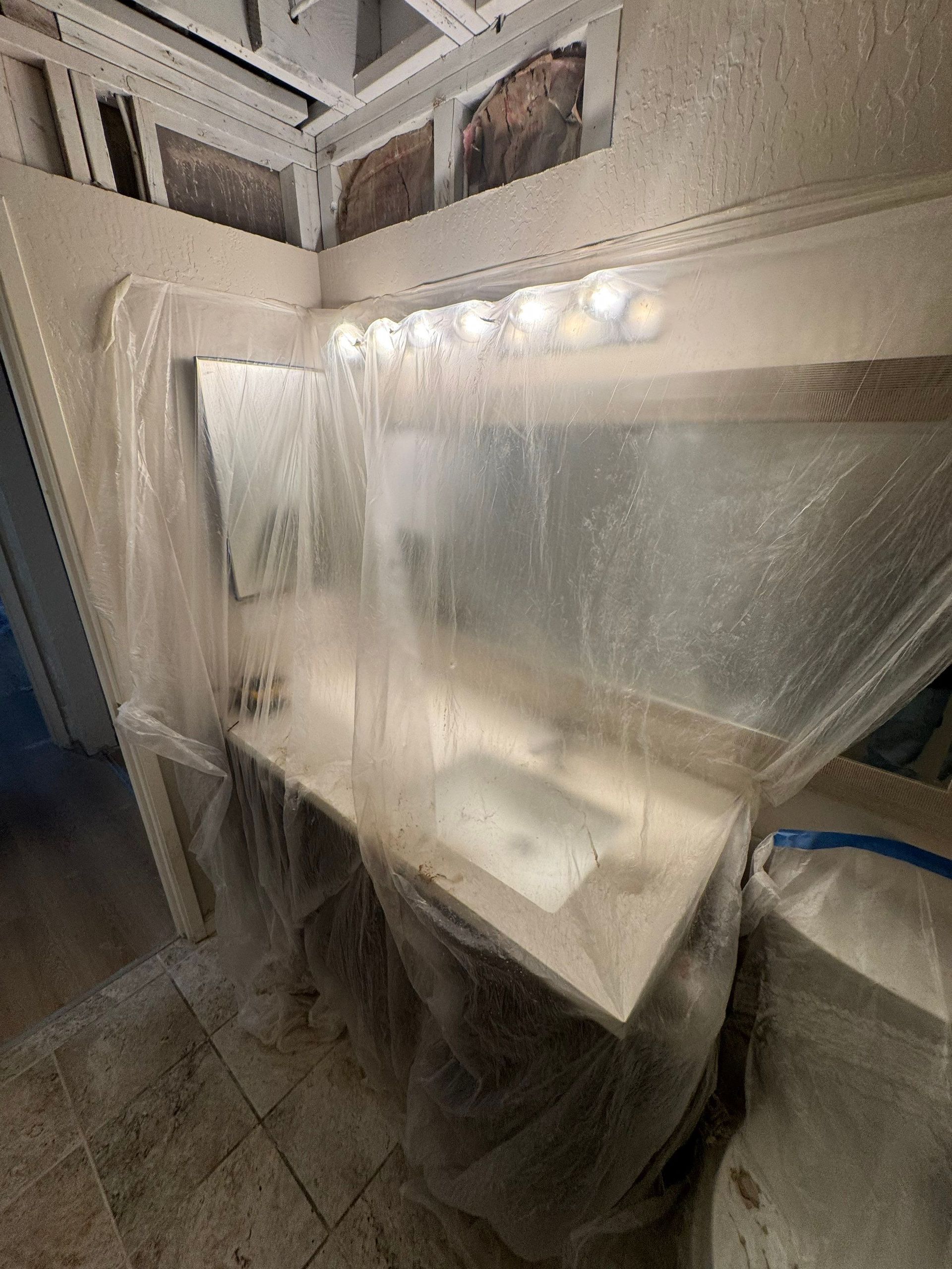 Bathroom sink and mirror covered with clear plastic sheeting, with lights above and tiled floor below