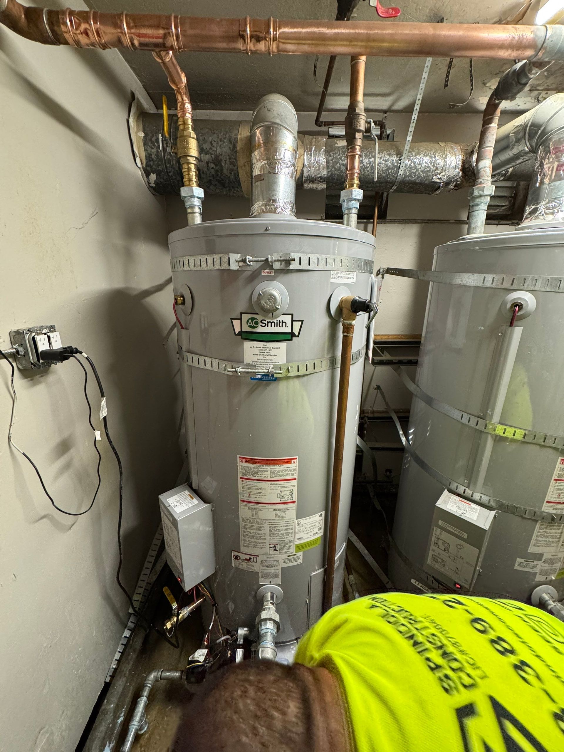 Basement utility room with water heater, pipes, and a yellow insulation-covered tank.