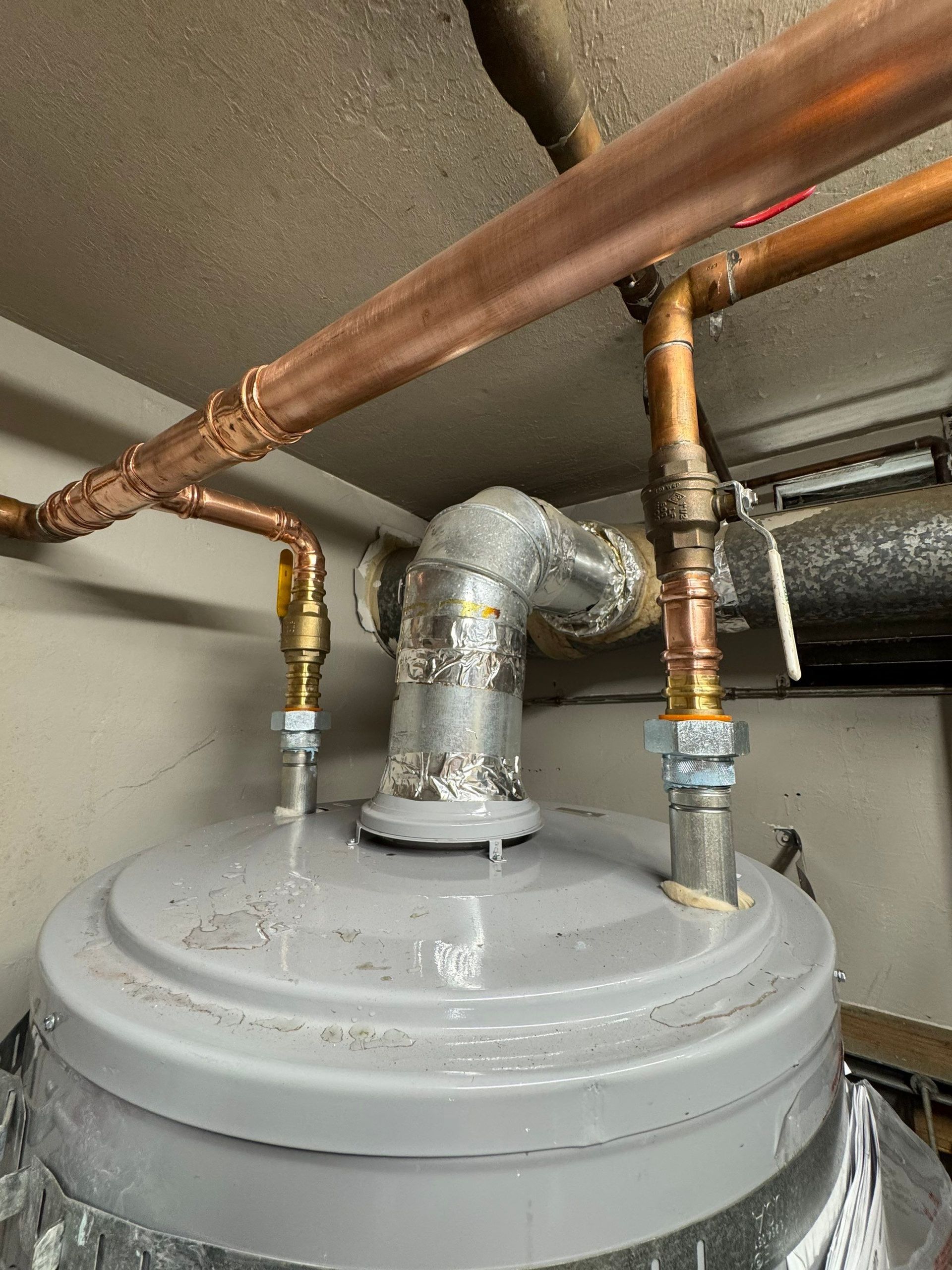 Close-up of corroded copper pipes and a damp wooden wall inside a cramped utility space