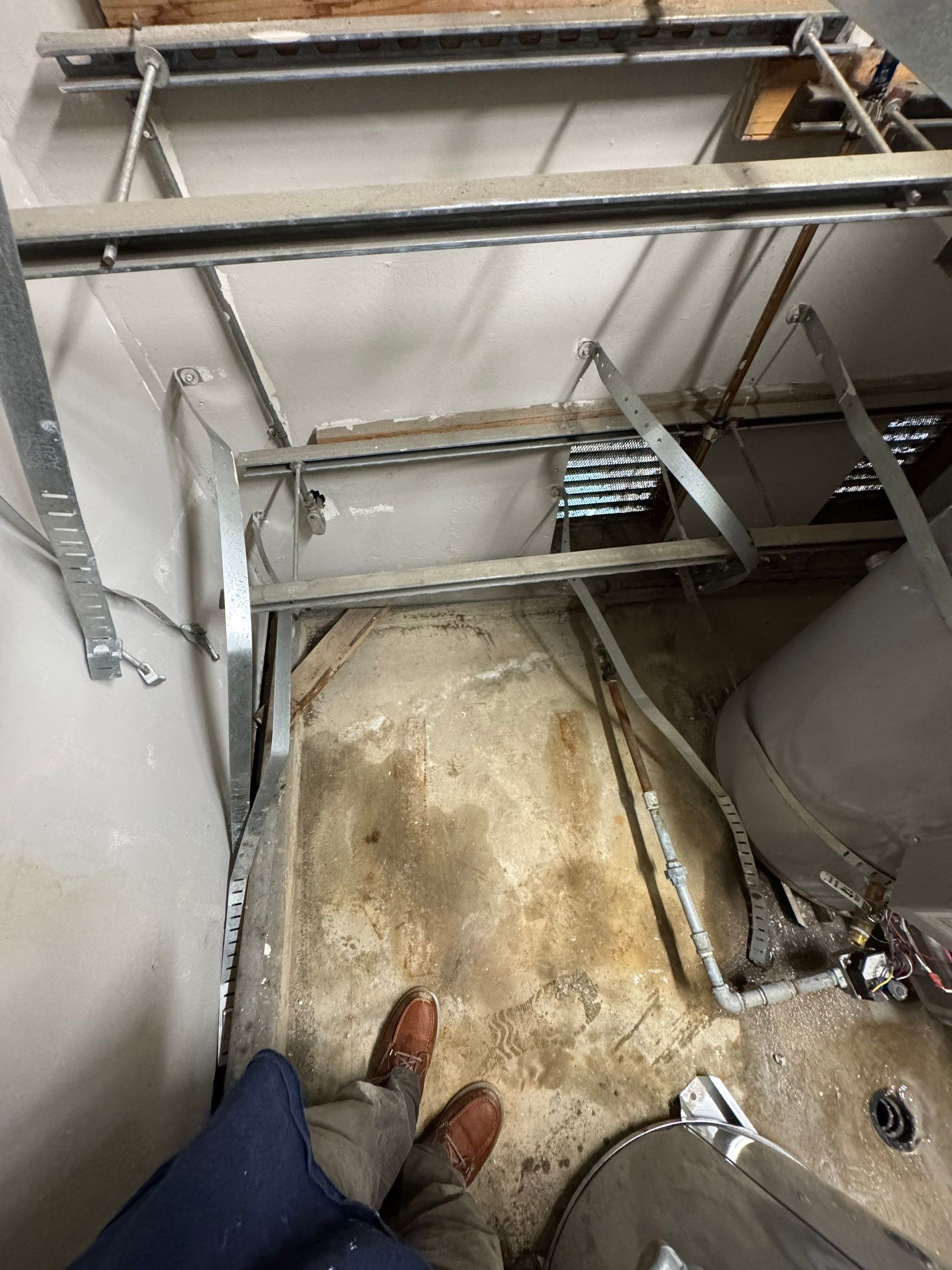 Exposed plumbing and pipes inside a wall opening above a baseboard, with wood framing and drywall cutout.