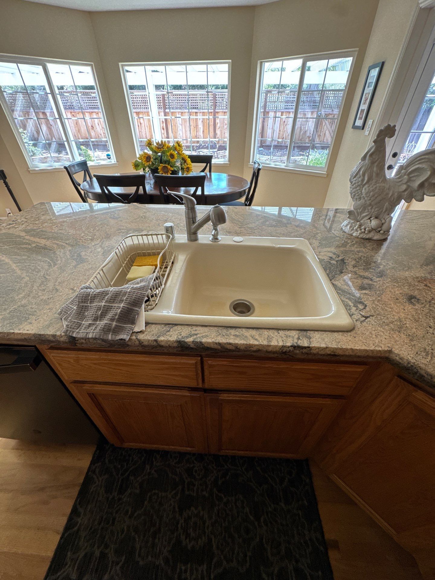 Kitchen sink with granite countertop and bright bay windows overlooking a dining table.