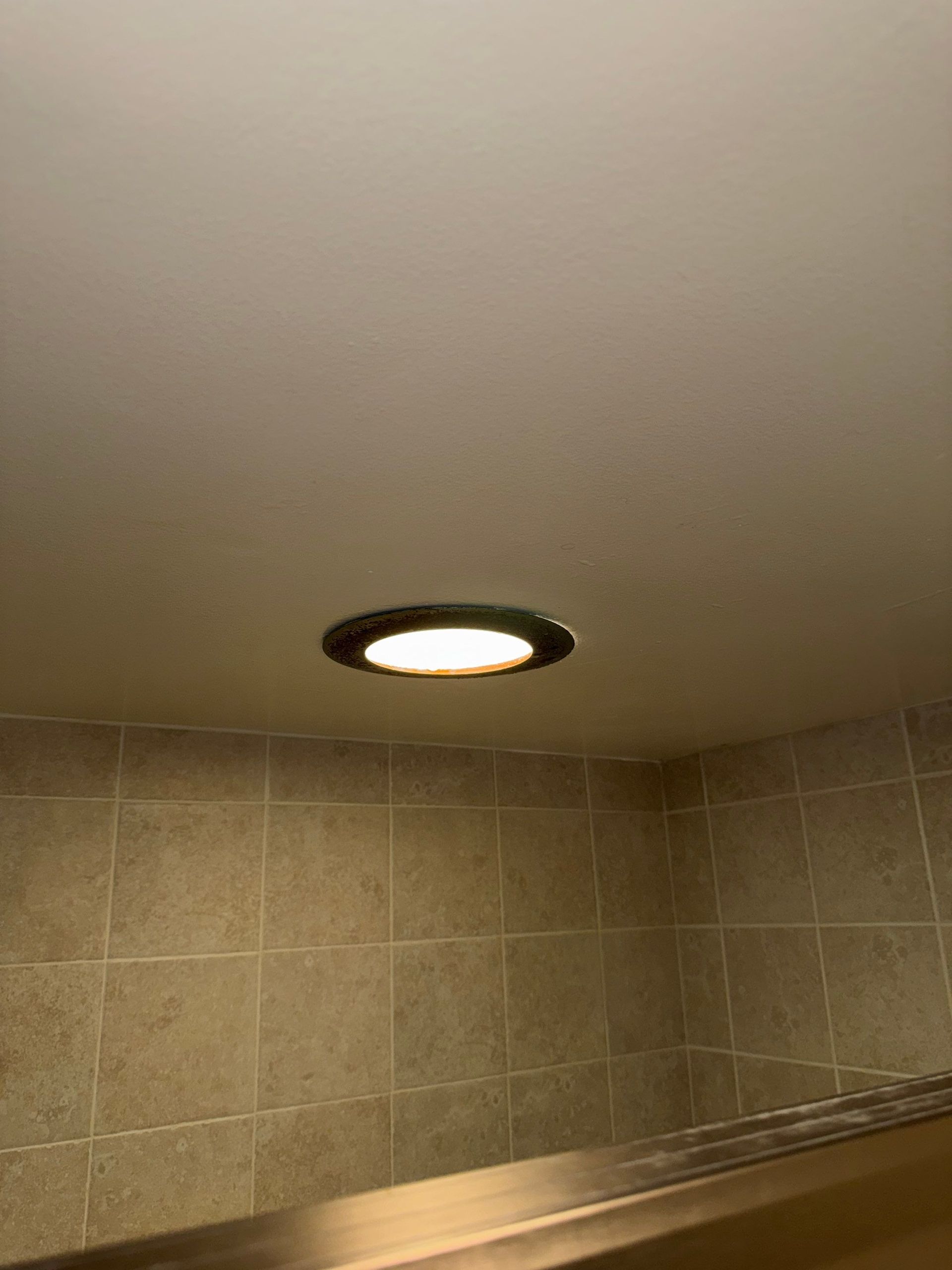Bathroom ceiling with recessed light above beige tiled wall and glass shower partition