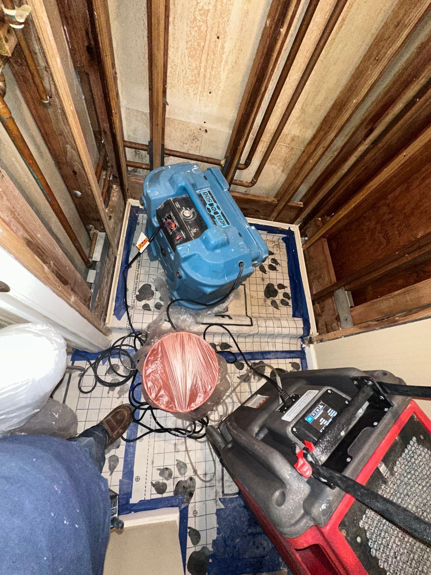 Cluttered utility closet with tools, cords, and a blue machine on a dusty floor.
