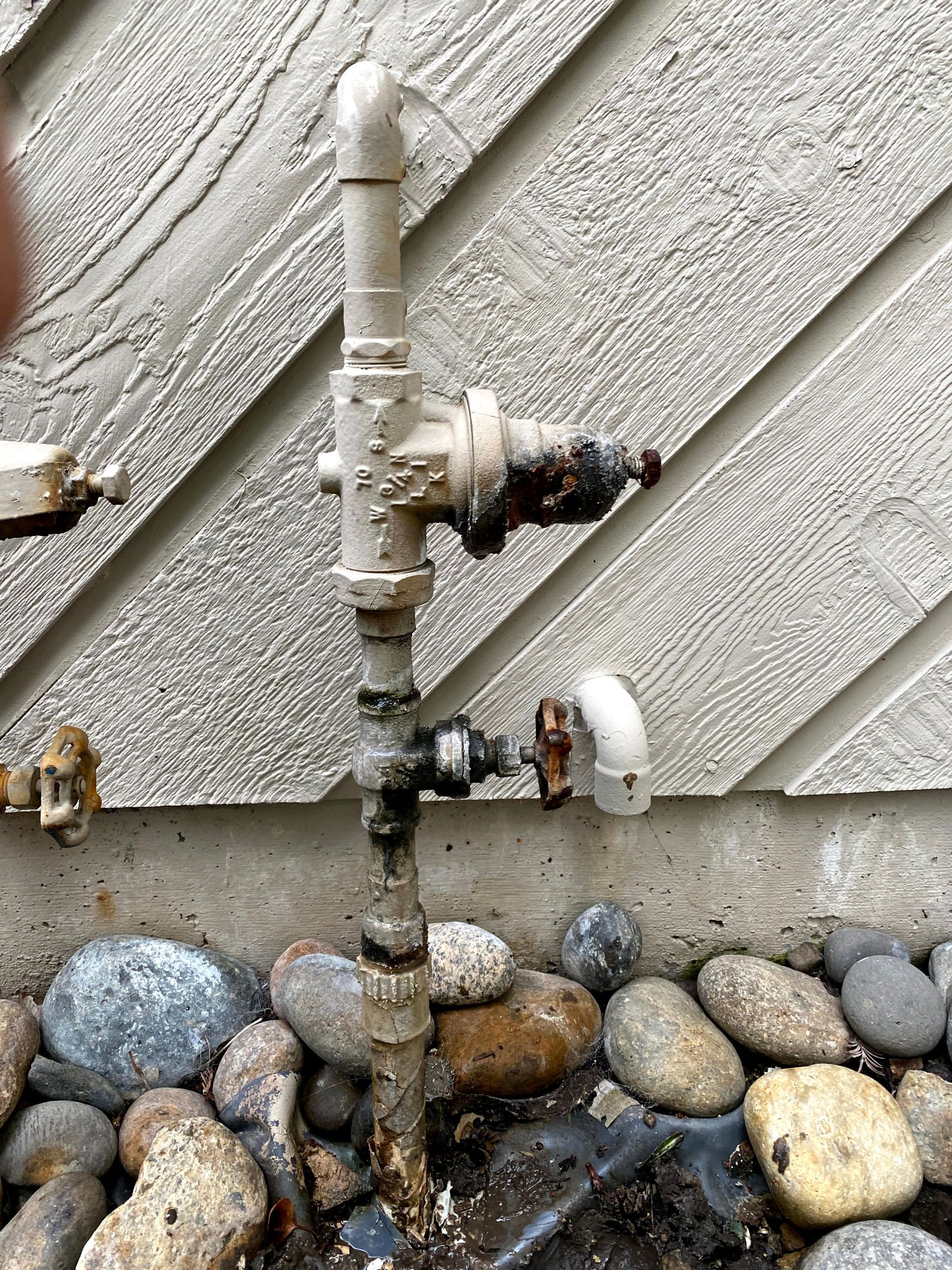 Close-up of a rusty metal pipe inside a parking lot, with cars in the background.