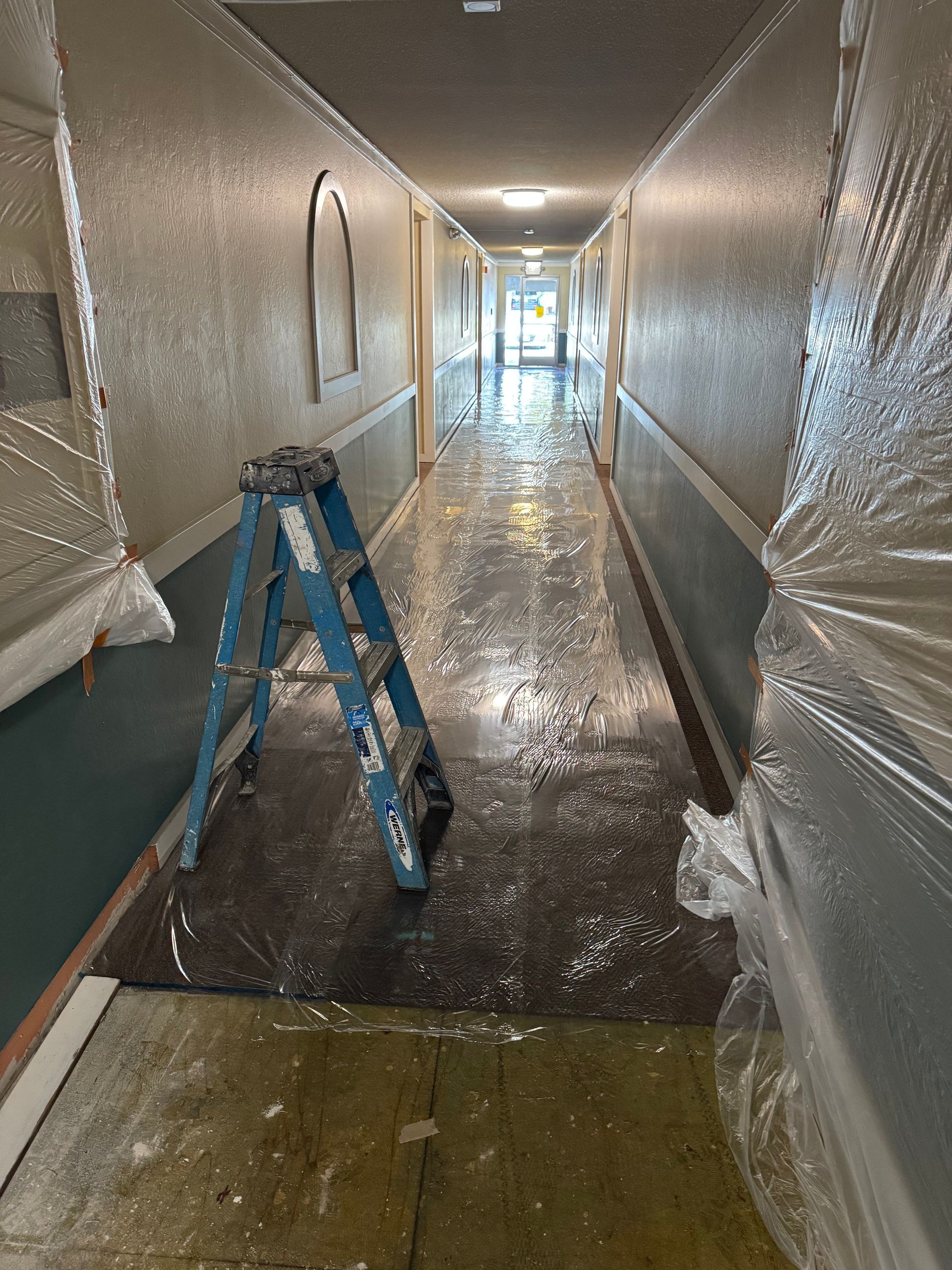 Hallway under renovation with a blue ladder and plastic sheeting along the walls and floor