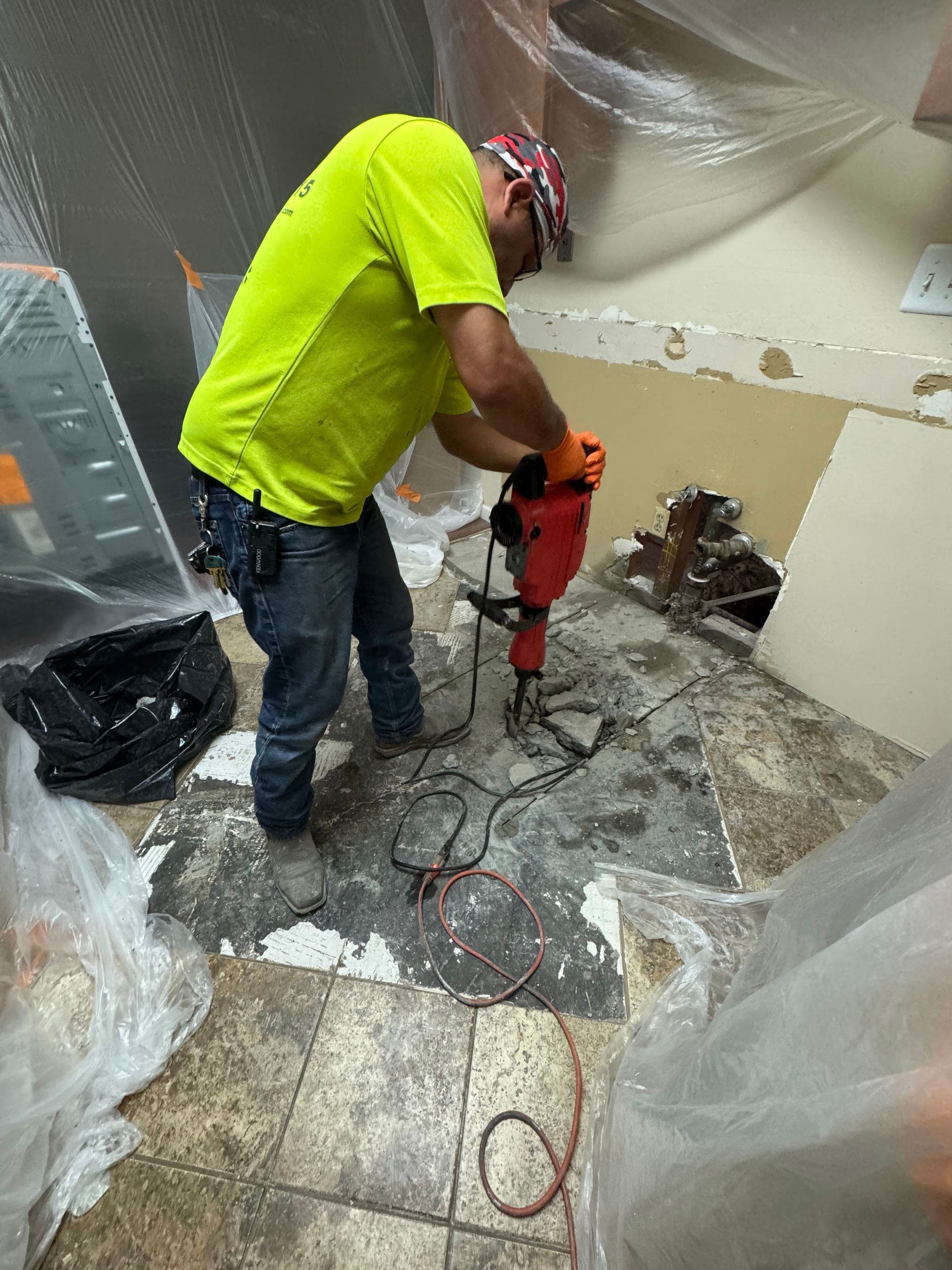 Worker in neon shirt using a jackhammer on a concrete floor during demolition work