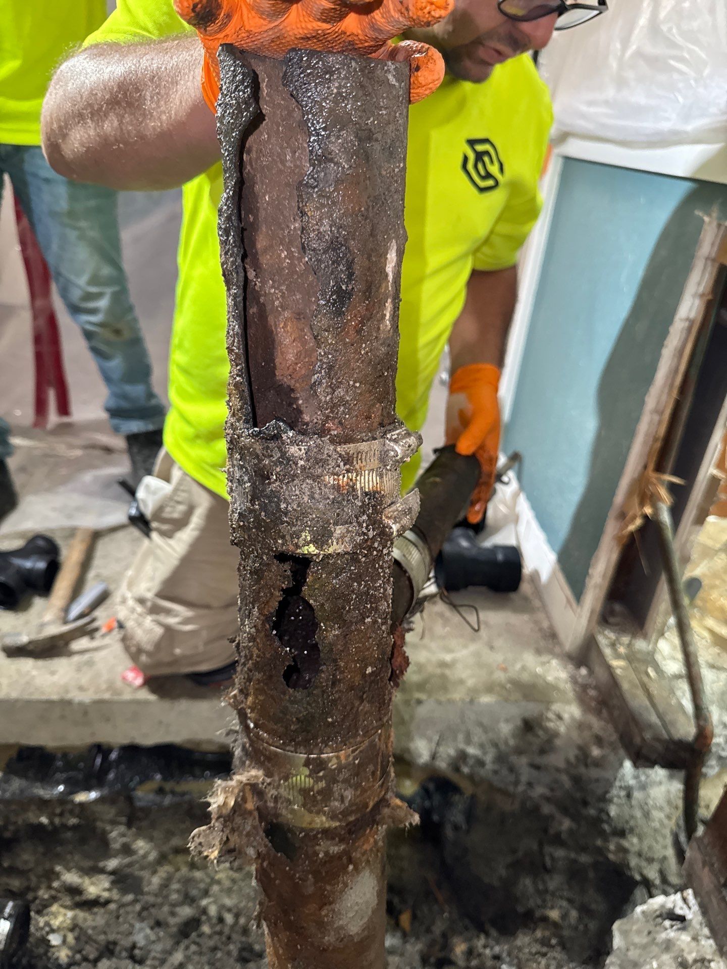 Worker holding a heavily rusted, corroded metal pipe in an industrial setting