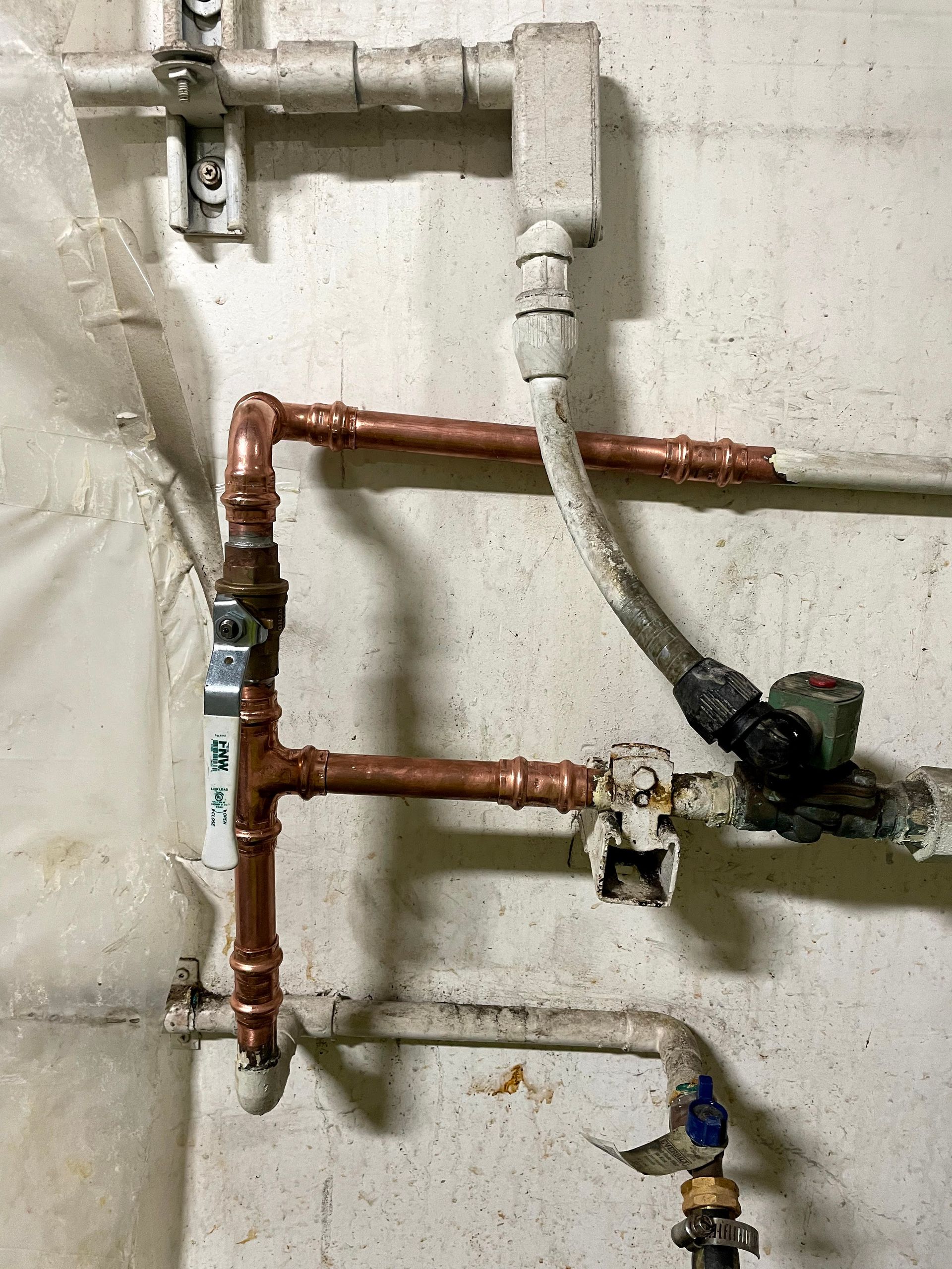 Plumbing valves and hoses with red, blue, and orange handles on a floor near a wall threshold
