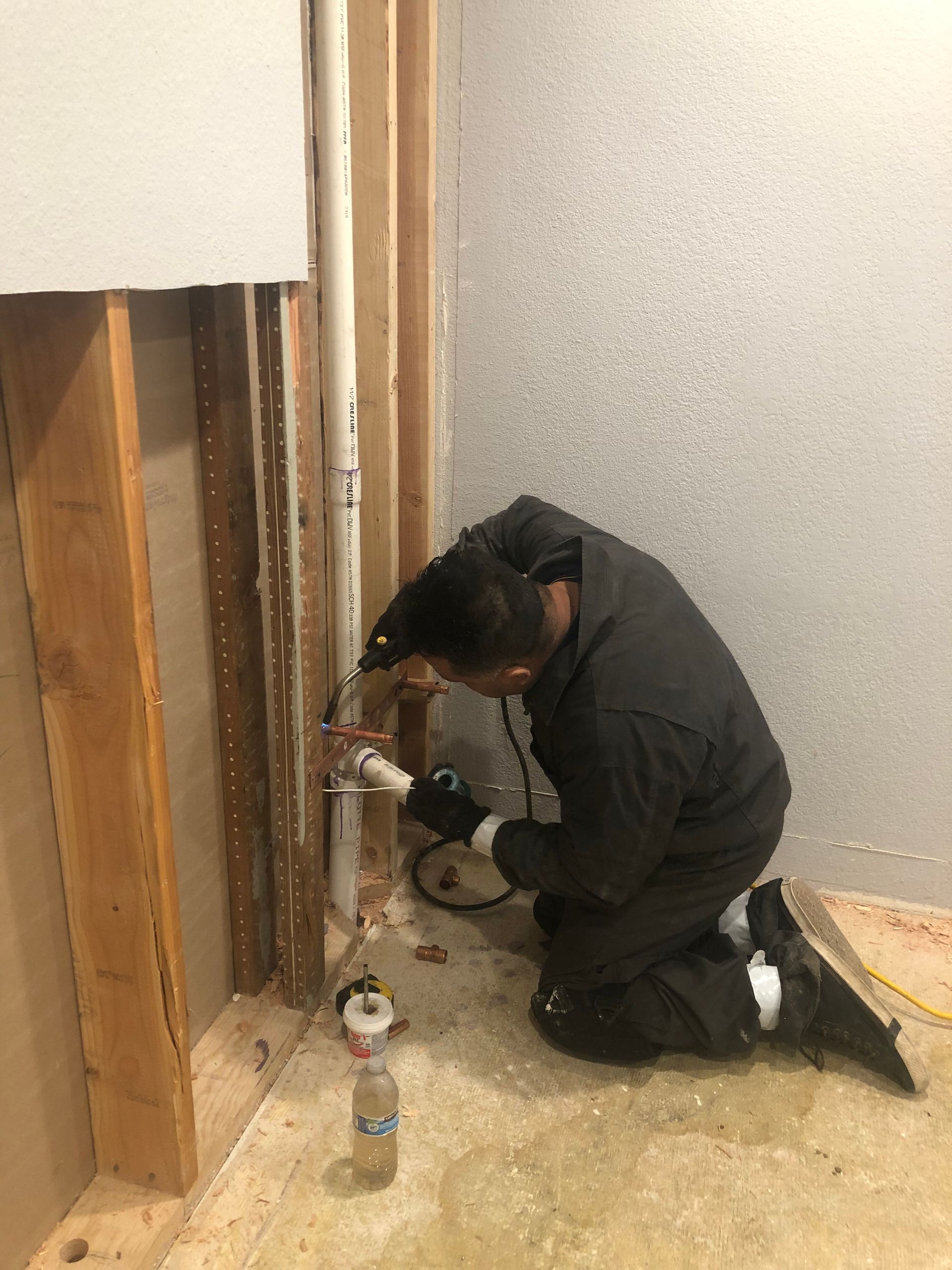Exposed wooden wall boards with plumbing pipes and rubble in a basement crawl space