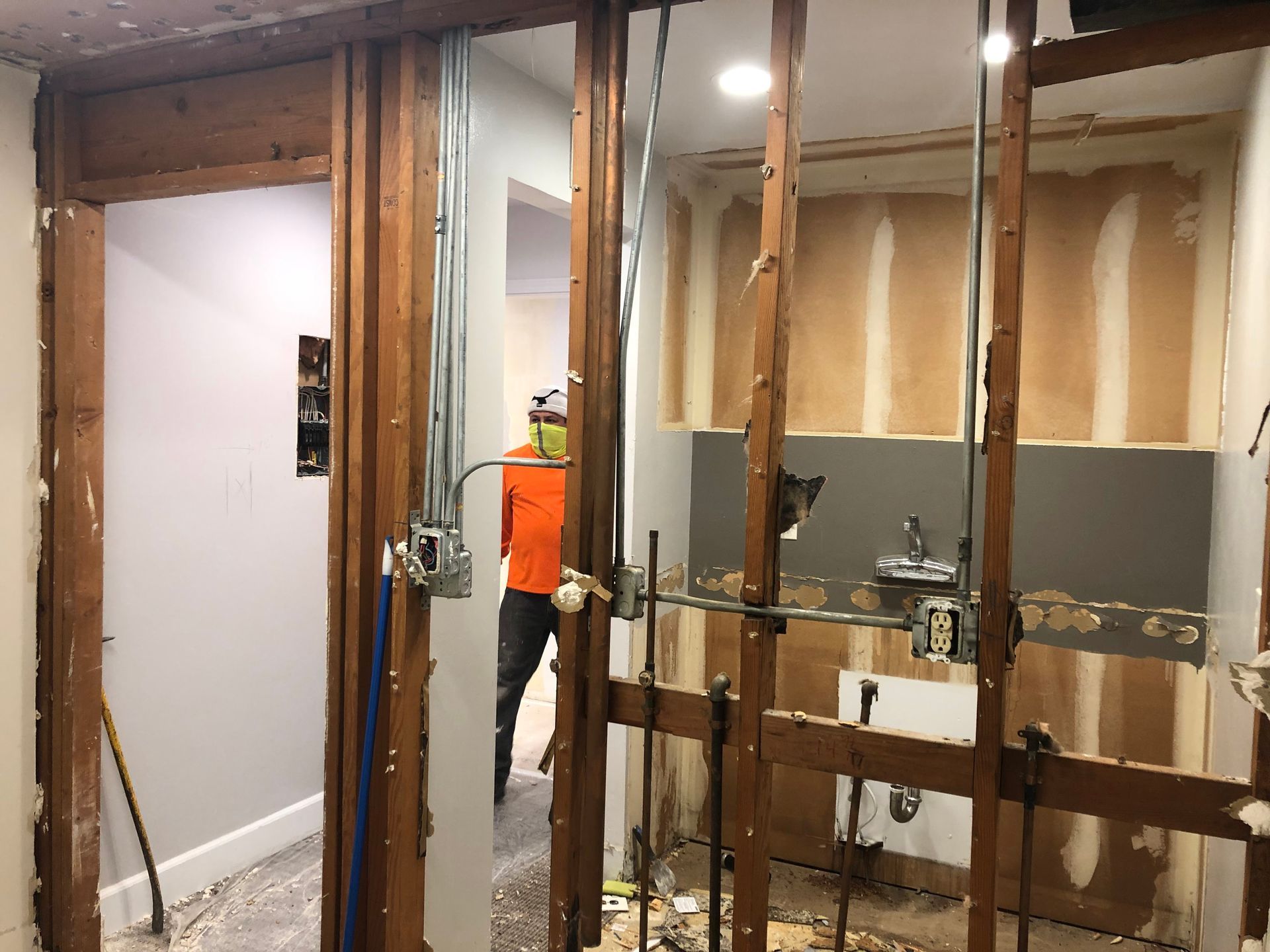 Bathroom renovation with exposed wall studs and a worker in an orange vest near the doorway