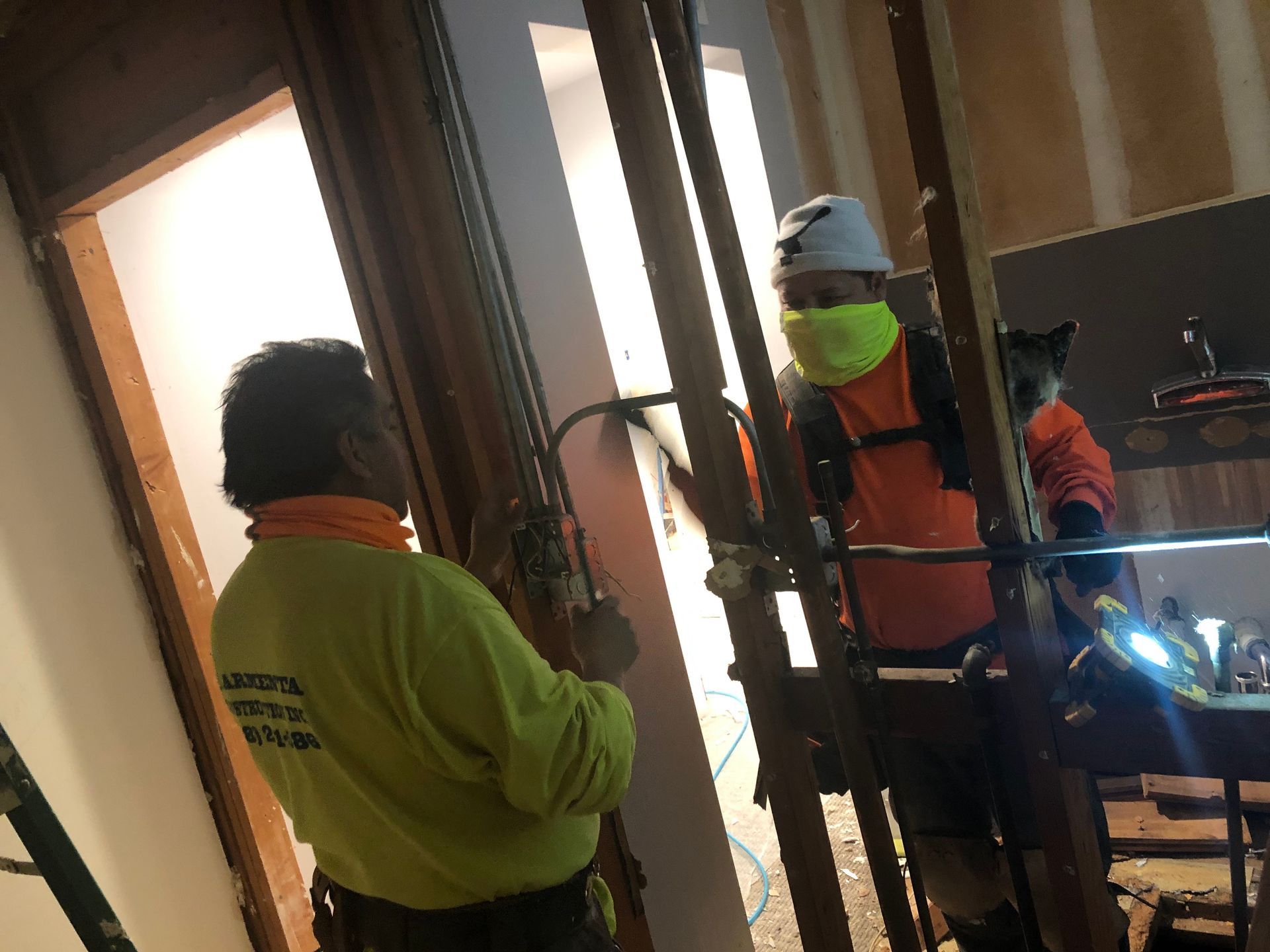 Workers in reflective jackets and helmets install wiring in a narrow indoor hallway.