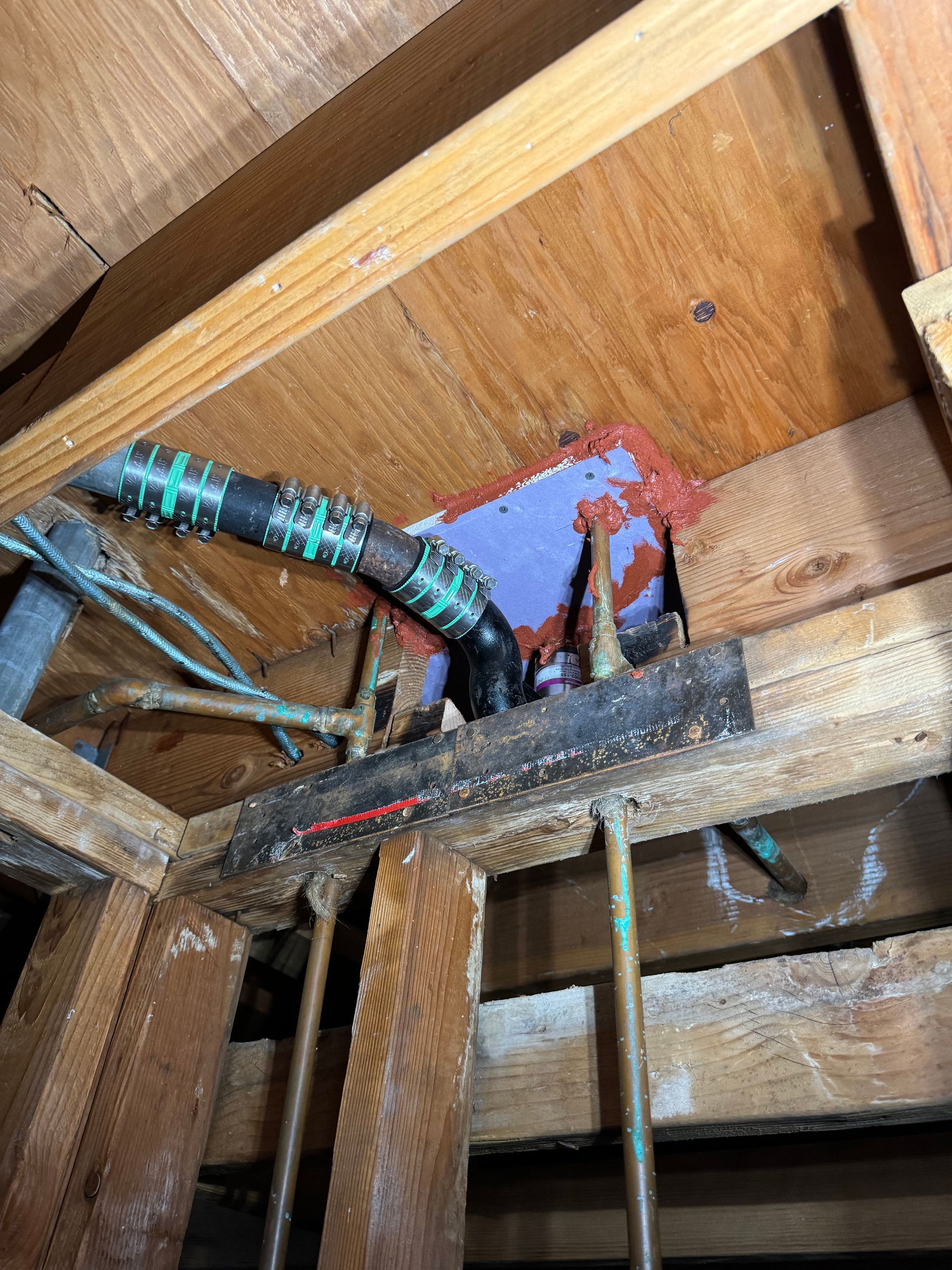 Electrical cables in a wooden attic opening, with red, blue, and black wires exposed.