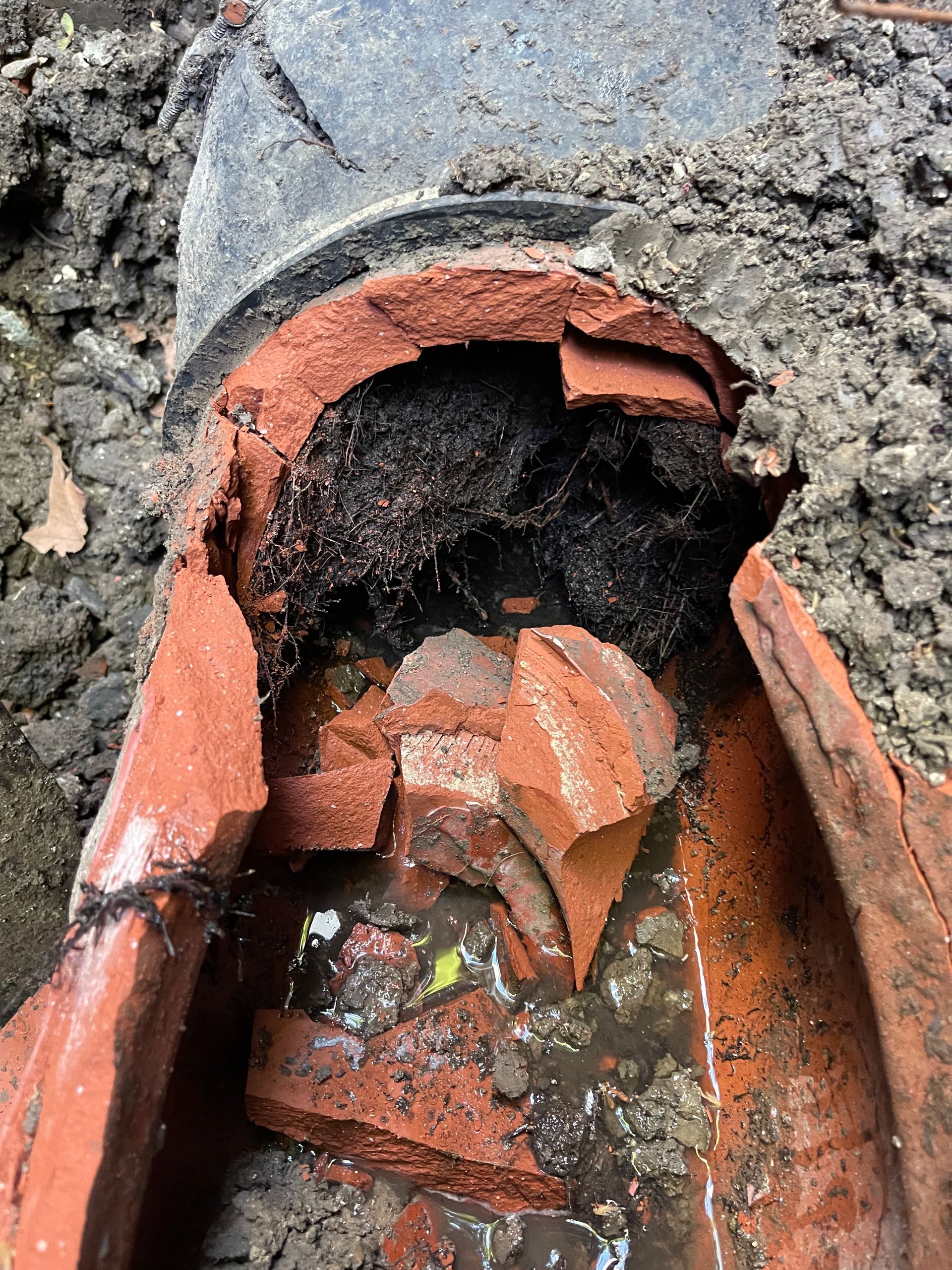 Broken terracotta pipe in a wet stone surface, with dark debris and pooled water inside.