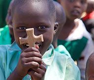 A young boy is holding a wooden cross in front of his face.