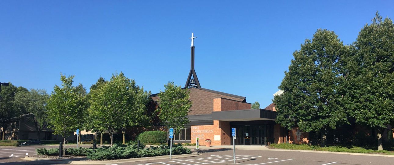 A church with a cross on top is surrounded by trees and a parking lot.