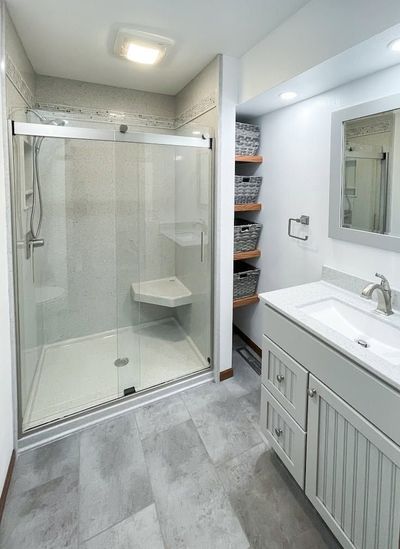 Bright bathroom with glass shower, vanity sink, mirror, and gray tile flooring.