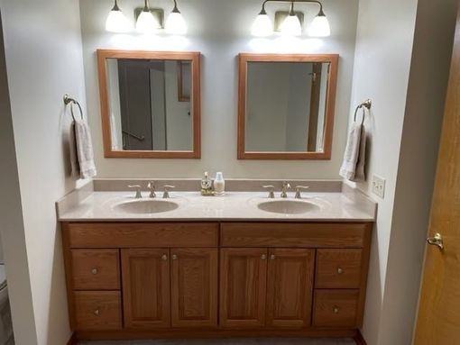 Bathroom vanity with double sinks, wood cabinets, mirrors, and wall sconces.