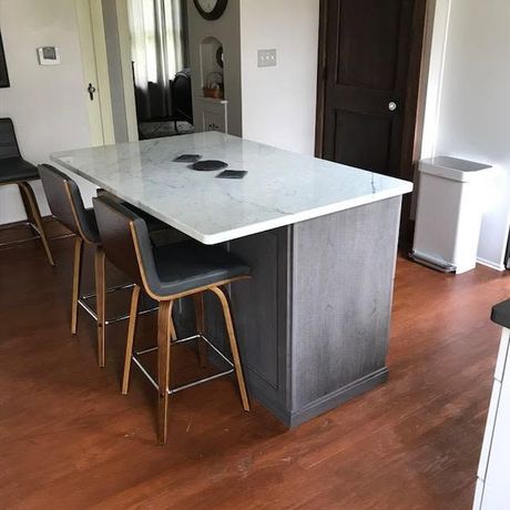 Modern kitchen with a white island, dark cabinets, and two stools on wood flooring