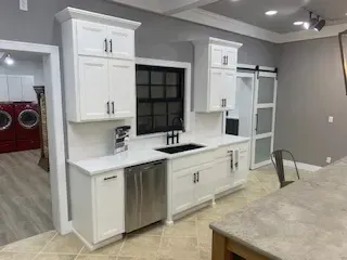 Bright white kitchen cabinets and sink with stainless dishwasher beside a gray dining area.