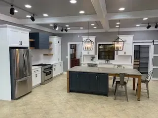 Modern kitchen with white cabinets, stainless appliances, teal island, and two hanging lantern lights.