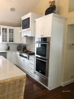 Bright white kitchen with built-in stainless steel ovens and a cat sitting atop the cabinets
