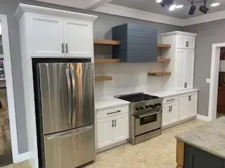 Modern kitchen with stainless steel appliances, white cabinets, open wooden shelves, and gray backsplash
