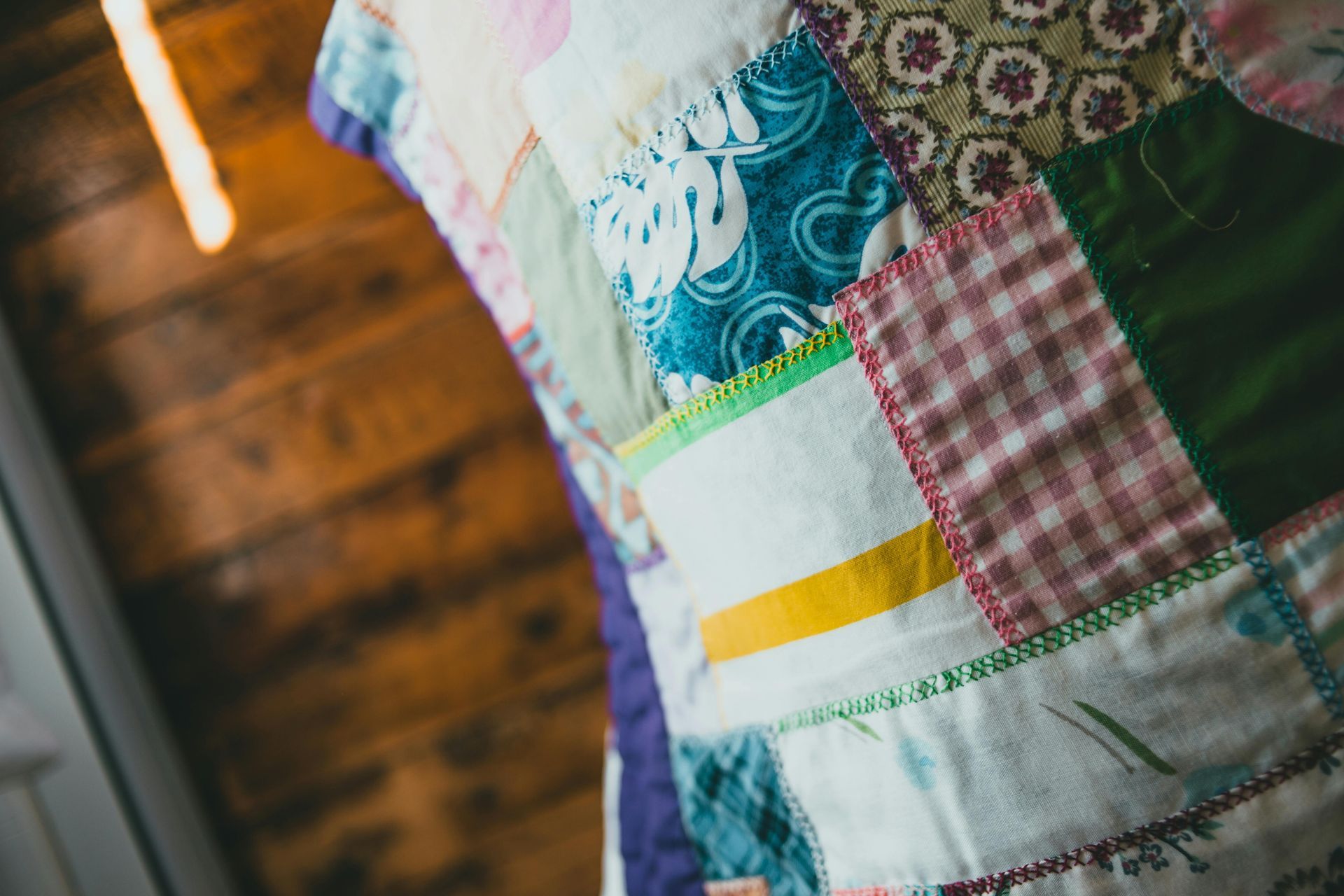 A close-up of a colorful, hand-stitched patchwork quilt with varied patterns and textures, set against wooden walls.