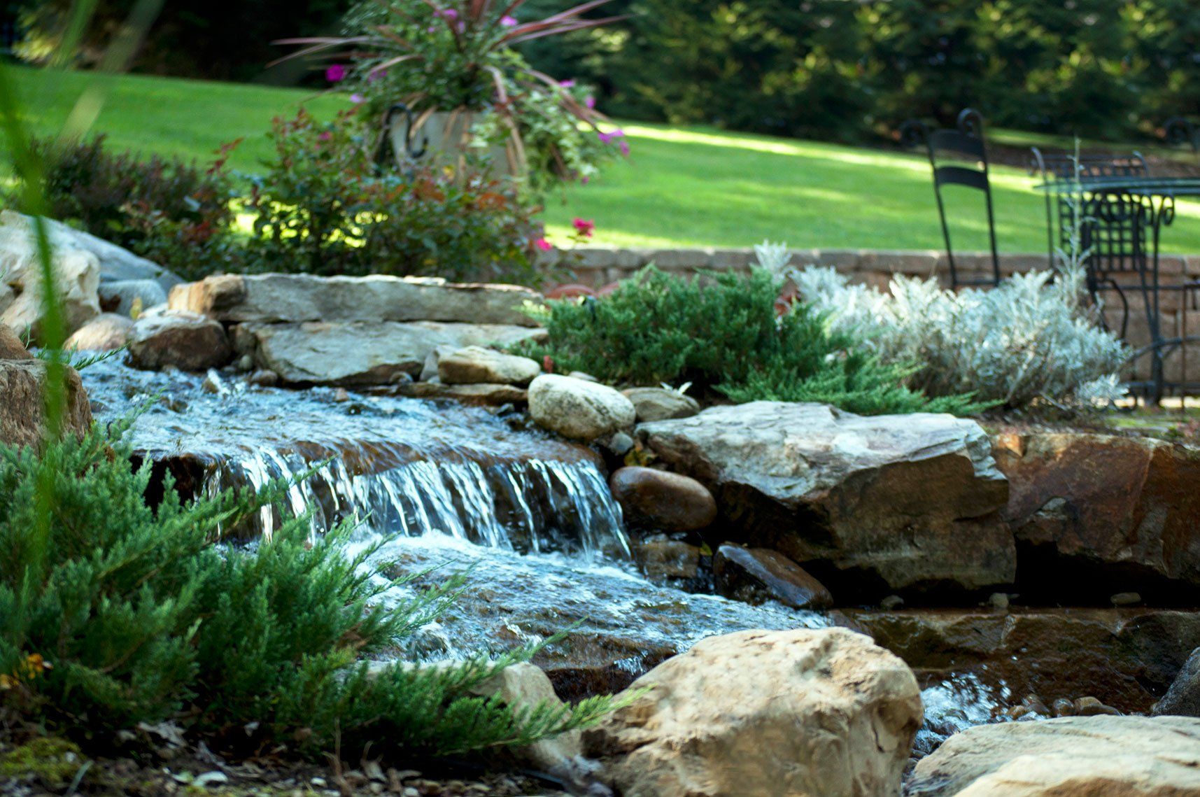 Residential waterfall with levels, natural landscape rocks, and evergreens