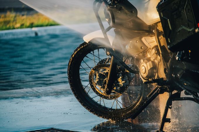 La ruota anteriore di una motocicletta schizza acqua su una strada bagnata al tramonto.