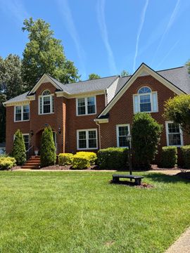 Brick suburban house with manicured lawn, white trim, and clear blue sky