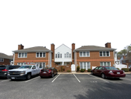 Apartment building with parked cars in front and white trim, viewed from a parking lot.