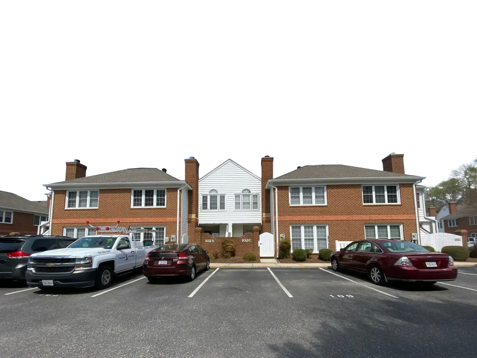 Apartment building with parked cars in front and white trim, viewed from a parking lot.