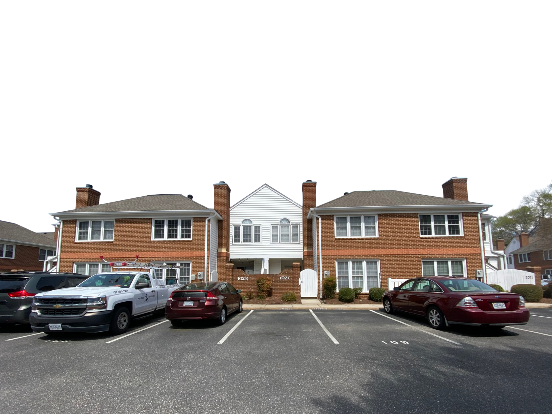 Apartment building with parked cars in front and white trim, viewed from a parking lot.