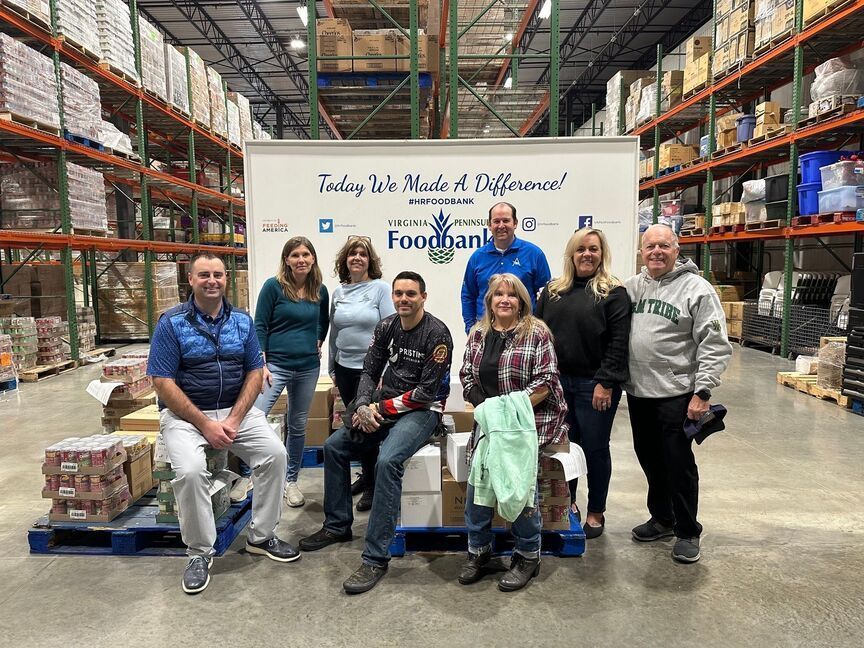 Group of people posing in a warehouse with stacked pallets and a donation banner behind them.