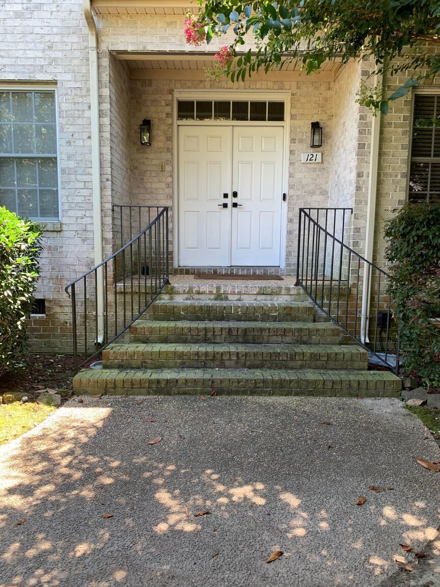 Front entrance with white double doors, stone steps, black railings, and a gravel path under dappled sunlight