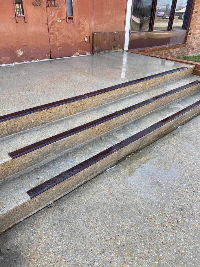 Concrete steps and a ramp beside a brick building entrance with a glass door