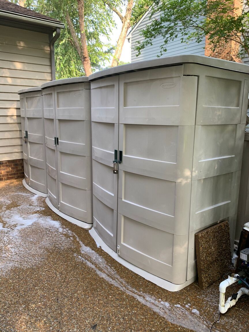 Large gray storage shed beside a house, with white foam insulation scattered around its base.