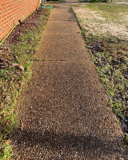 Concrete walkway beside a brick wall, bordered by grass and mulch in a yard