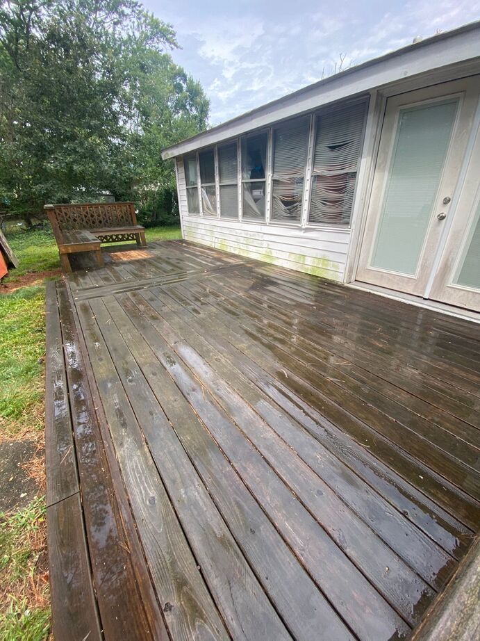 Rain-soaked wooden deck beside a house with screened windows and a bench in the yard